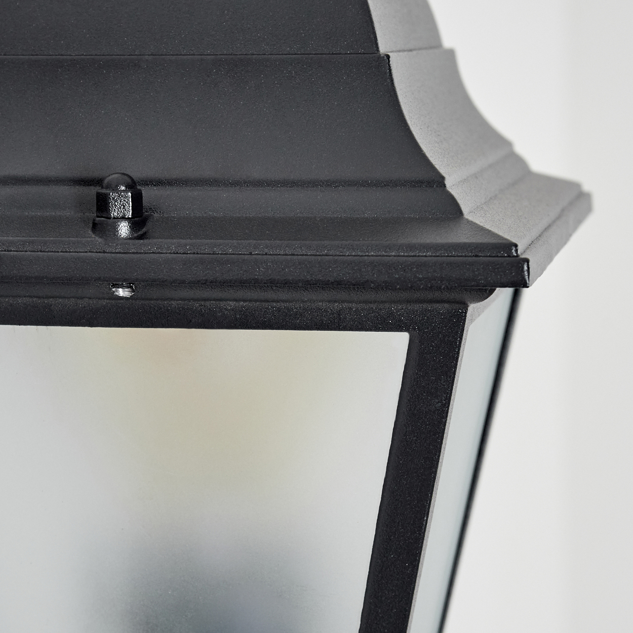 Nahaufnahme einer schwarzen Außenlampe. Die Lampe hat einen oberen Teil, eine Glasscheibe und einen Metallrahmen, vor weißem Hintergrund.