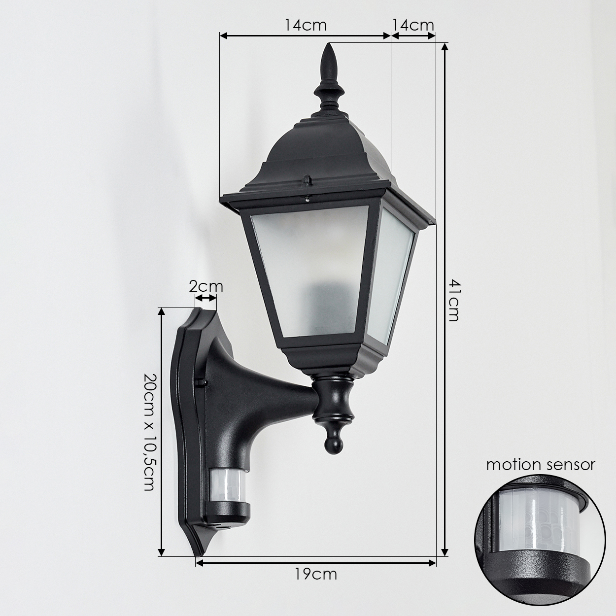 Schwarze Außenlampe mit Maßen und Bewegungsmelder, an weißer Wand montiert. Sie hat Glasscheiben und eine dekorative Spitze.