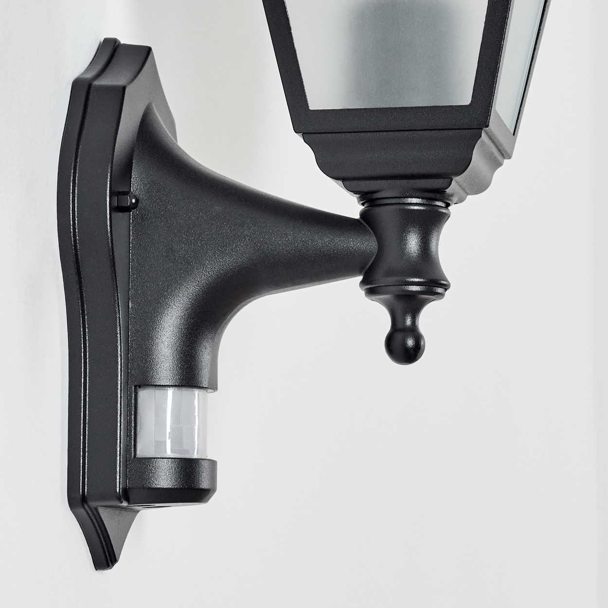 Schwarze Außenlampe mit Bewegungsmelder an weißer Wand. Die Lampe ist klassisch mit Glasscheiben.