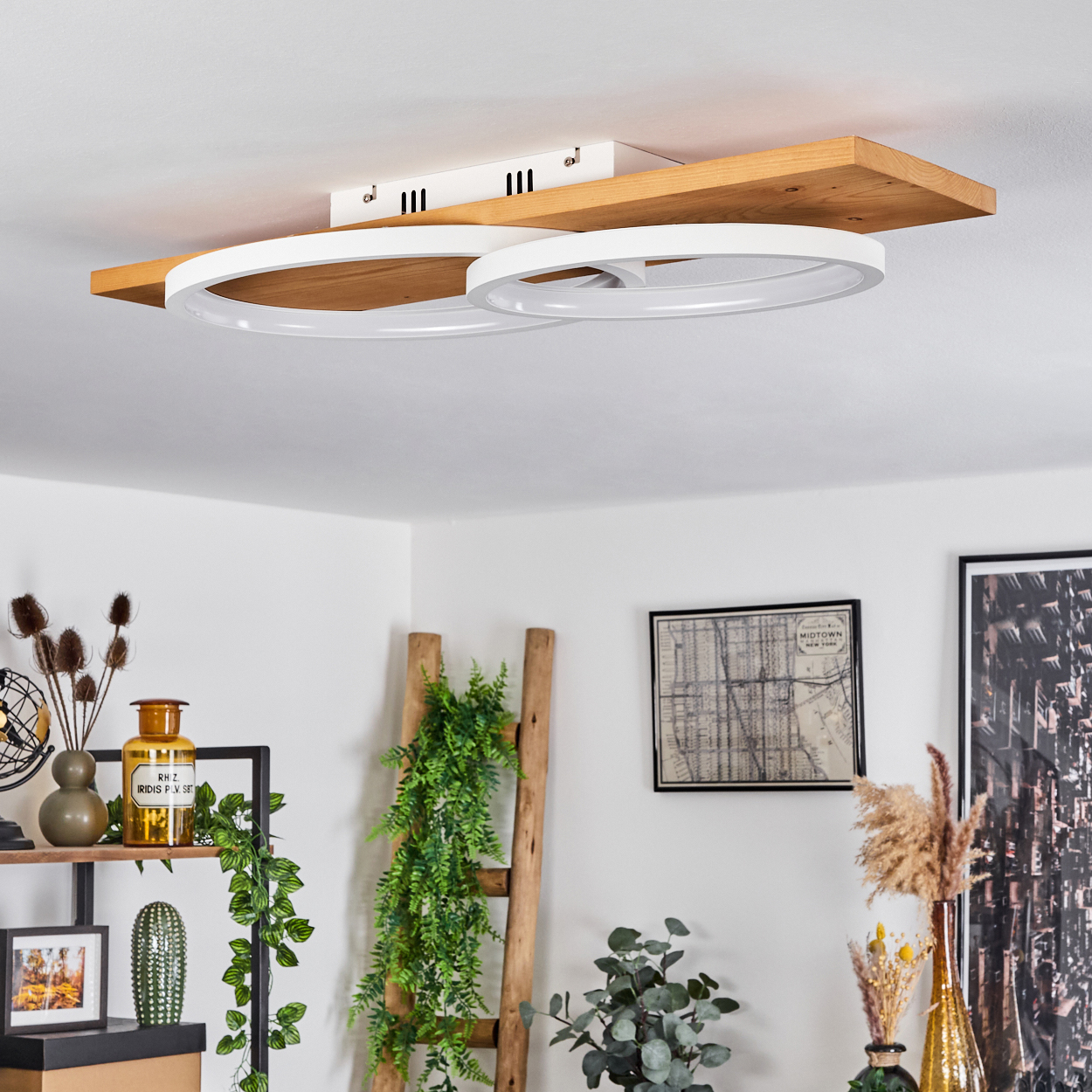 Eine moderne Deckenlampe mit zwei weißen Kreisen auf einem Holzbrett, umgeben von Dekorationsartikeln, Pflanzen und einer Leiter.