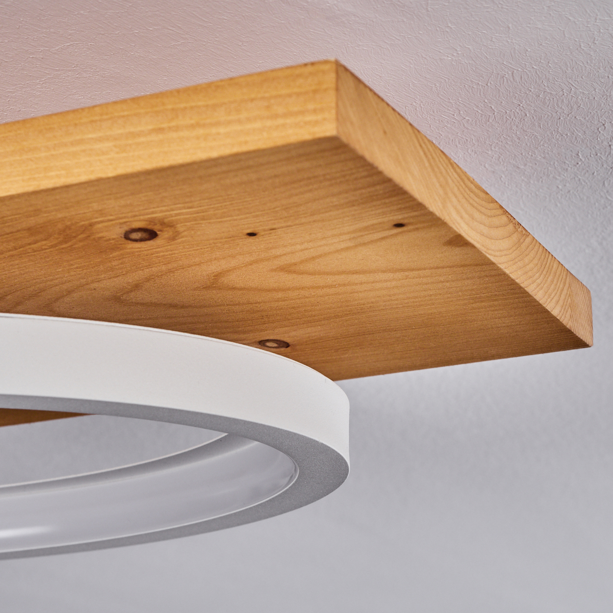 Ein Holzregal ist an einer strukturierten weißen Decke befestigt. Unter dem Regal befindet sich eine weiße, ovale Leuchte.