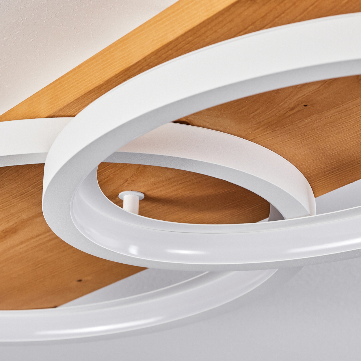 Nahaufnahme einer modernen Deckenleuchte. Weißes, geschwungenes Design über Holzpaneelen. Die Leuchte ist minimalistisch und elegant.