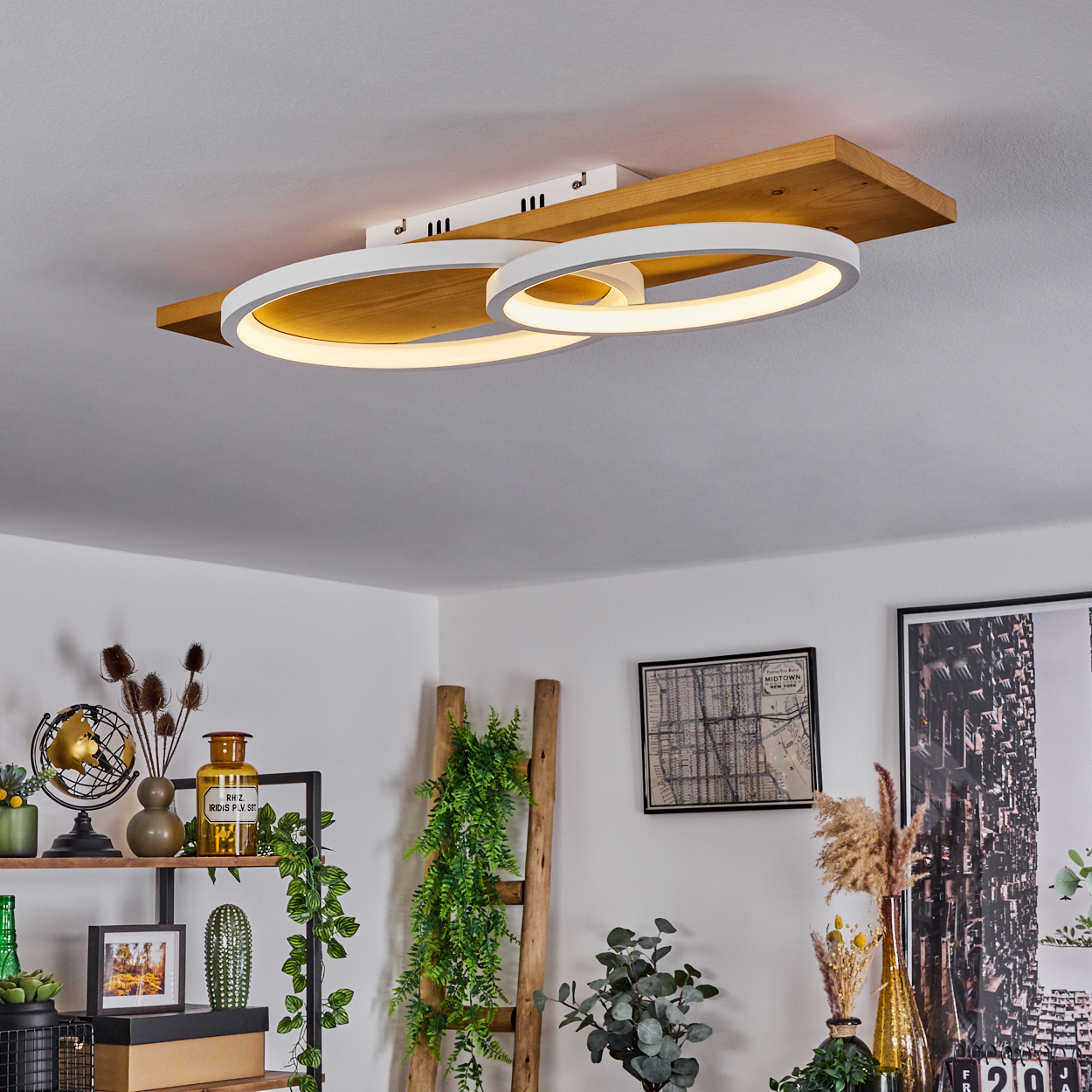 Eine moderne Deckenleuchte mit zwei weißen, kreisförmigen Lichtern sitzt auf einem Holzbrett. Der Raum hat auch Dekoration und eine Leiter.