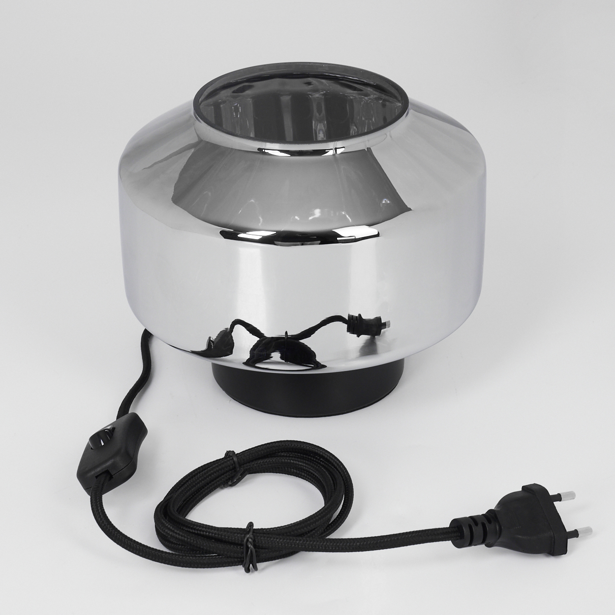 Verchromte Lampe auf weißem, rundem Sockel. Schwarzes Kabel mit Schalter und Stecker. Glänzende, reflektierende Oberfläche. Oberseite dunkel.