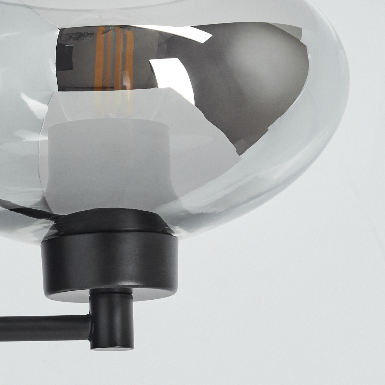 Nahaufnahme einer modernen Lampe. Eine graue Glaskugel mit einer Glühbirne im Inneren ist an einem schwarzen Metallrahmen befestigt.