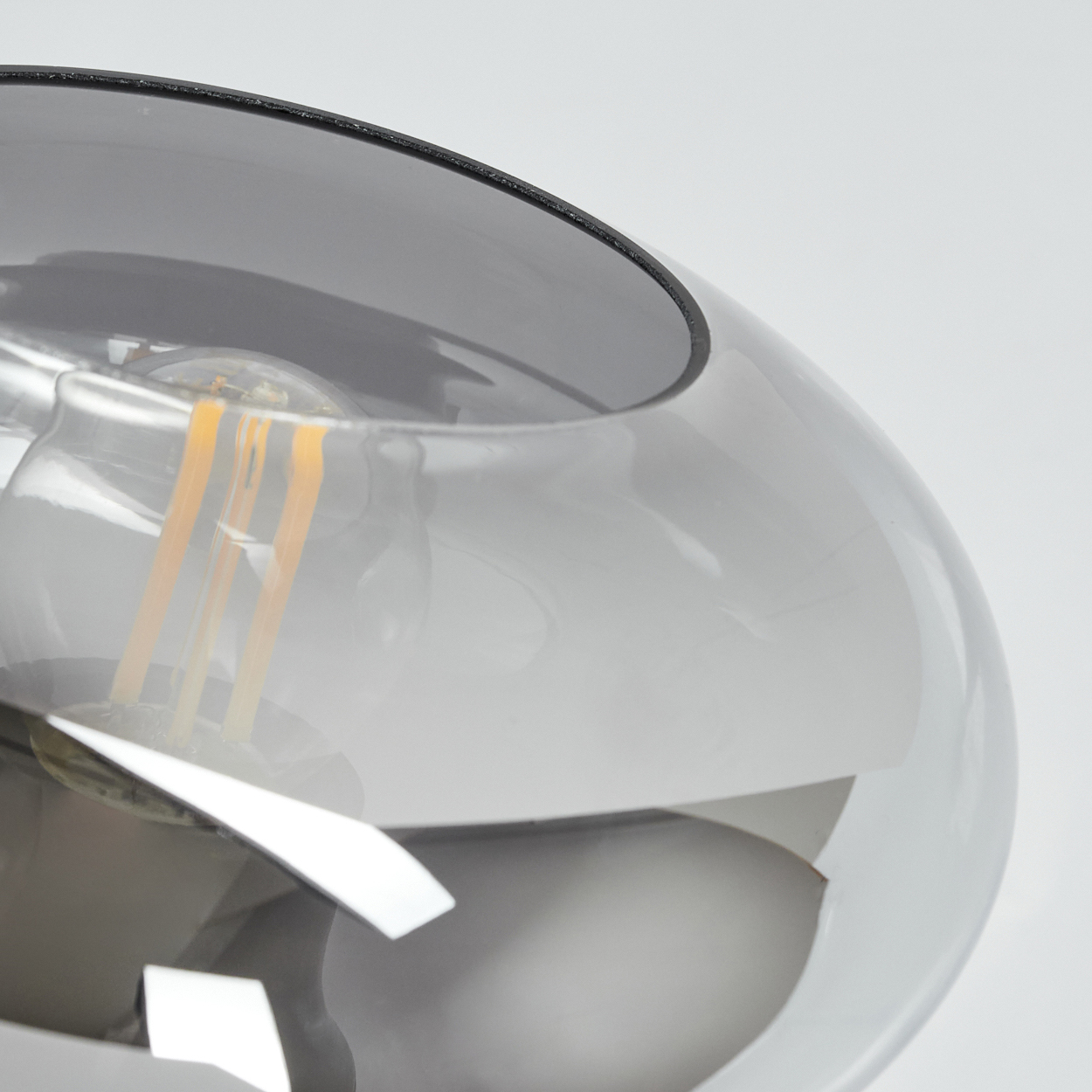 Nahaufnahme einer modernen Lampe mit grauem, abgerundetem Schirm. Die Glühbirne ist sichtbar. Der Hintergrund ist weiß.