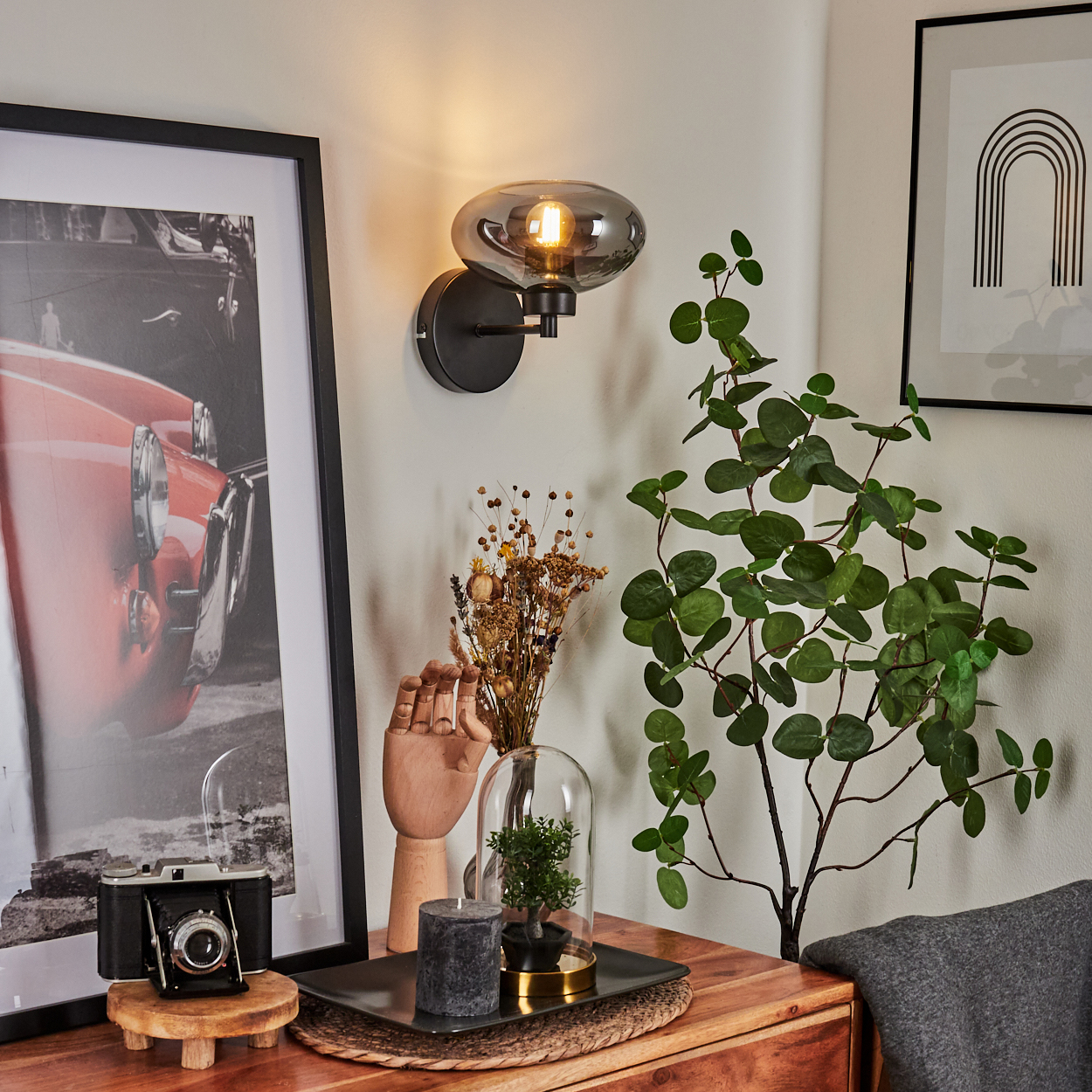 Ein Raum mit Lampe, Kunst, Pflanzen und Dekor auf einem Holztisch. Eine Vintage-Kamera steht auf einem Holzständer.