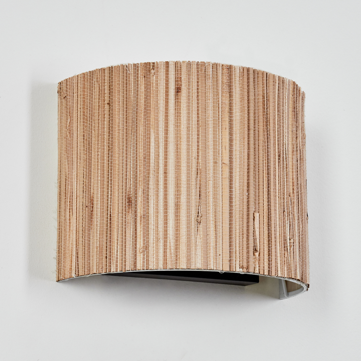 Eine gewebte, zylindrische Wandleuchte, beige und braun, an einer weißen Wand montiert. Die Lampe ist gewölbt und hat einen dunklen Sockel.