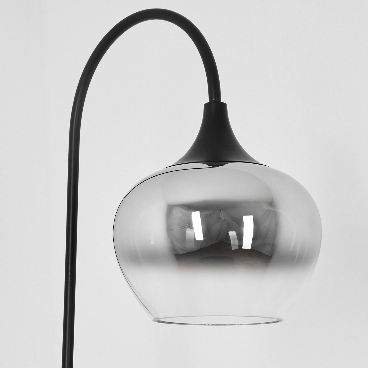Eine schwarze, bogenförmige Lampe mit Glasschirm. Der Schirm ist klar mit reflektierenden Eigenschaften. Der Hintergrund ist schlicht weiß.
