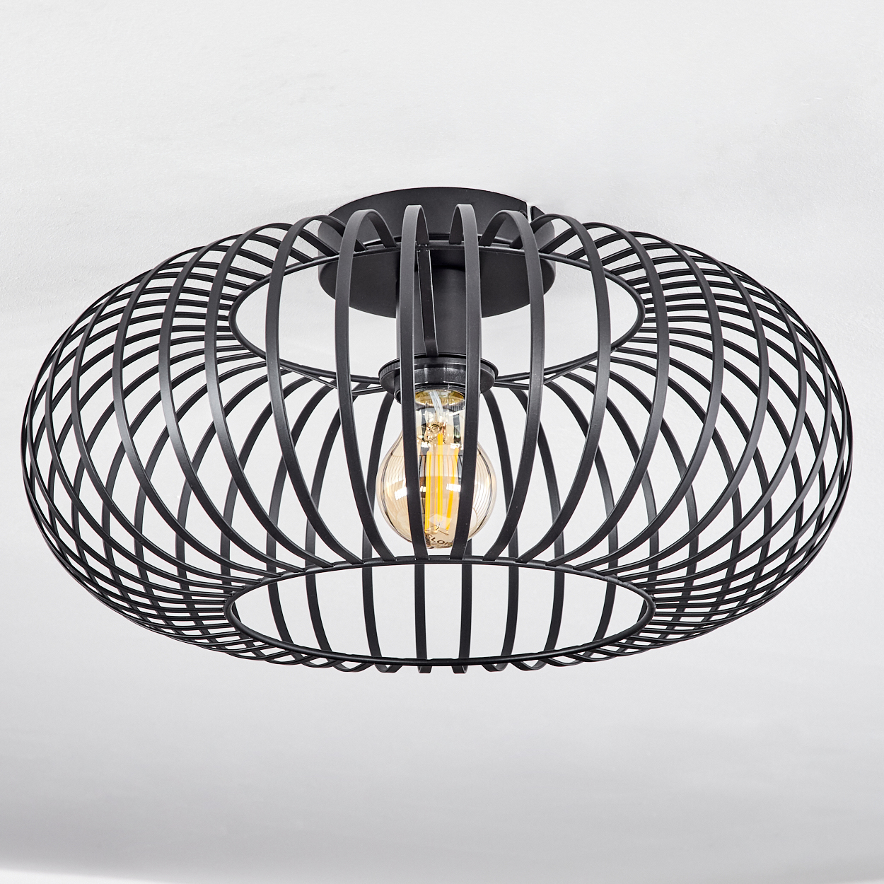 Eine schwarze, käfigartige Deckenlampe mit sichtbarer Glühbirne vor weißem Hintergrund.