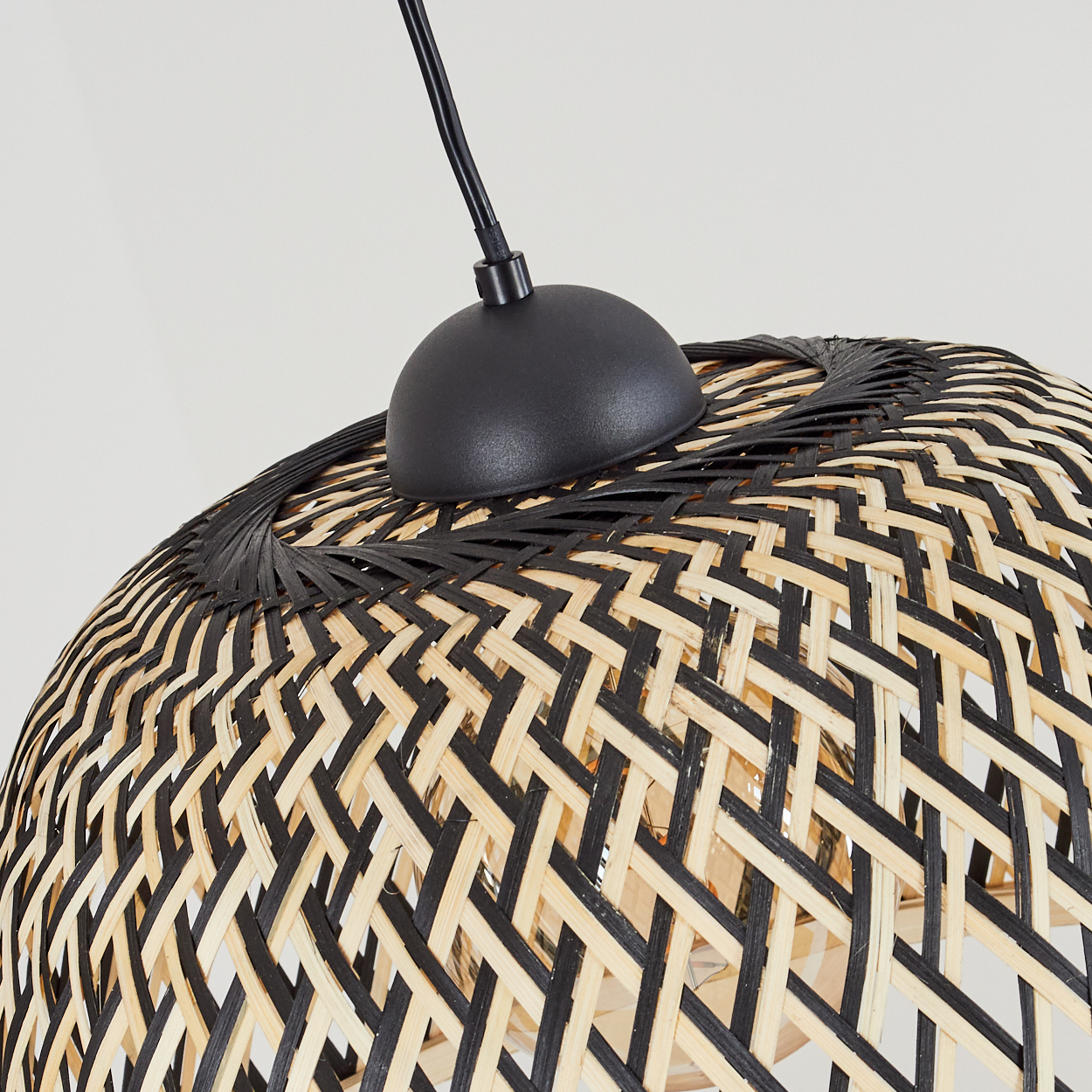 Nahaufnahme einer gewebten Lampe. Die Lampe hat einen schwarzen Sockel und ein gewebtes schwarz-beiges Muster. Ein schwarzes Kabel ist sichtbar.