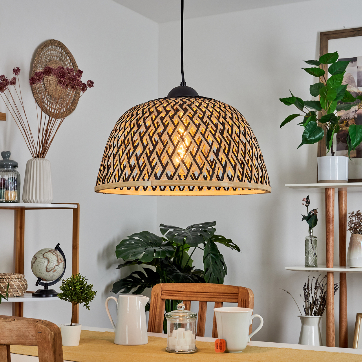 Ein Esszimmer mit gewebtem Lampenschirm, Pflanzen und einem für Tee gedeckten Tisch. Regale mit Dekorationsartikeln. Ein ruhiger, gut beleuchteter Raum.