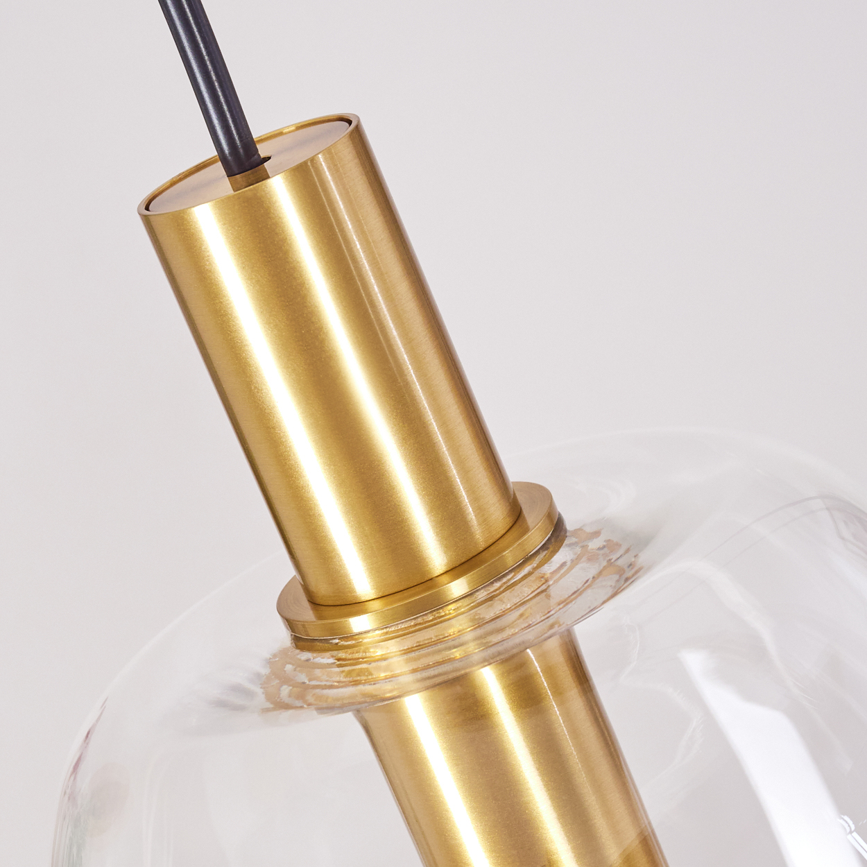 Nahaufnahme einer modernen Lampe. Sie hat eine zylindrische Armatur in Messingfarbe, die mit einer klaren Glaskugel verbunden ist. Ein schwarzes Kabel ragt von oben heraus.