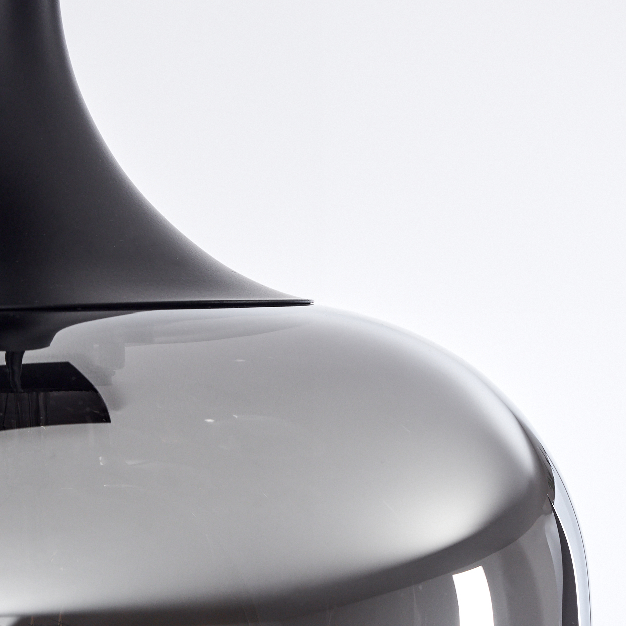 Nahaufnahme einer modernen Lampe. Die Oberseite ist schwarz, die Unterseite ein großes, graues, gebogenes Glas. Weißer Hintergrund.