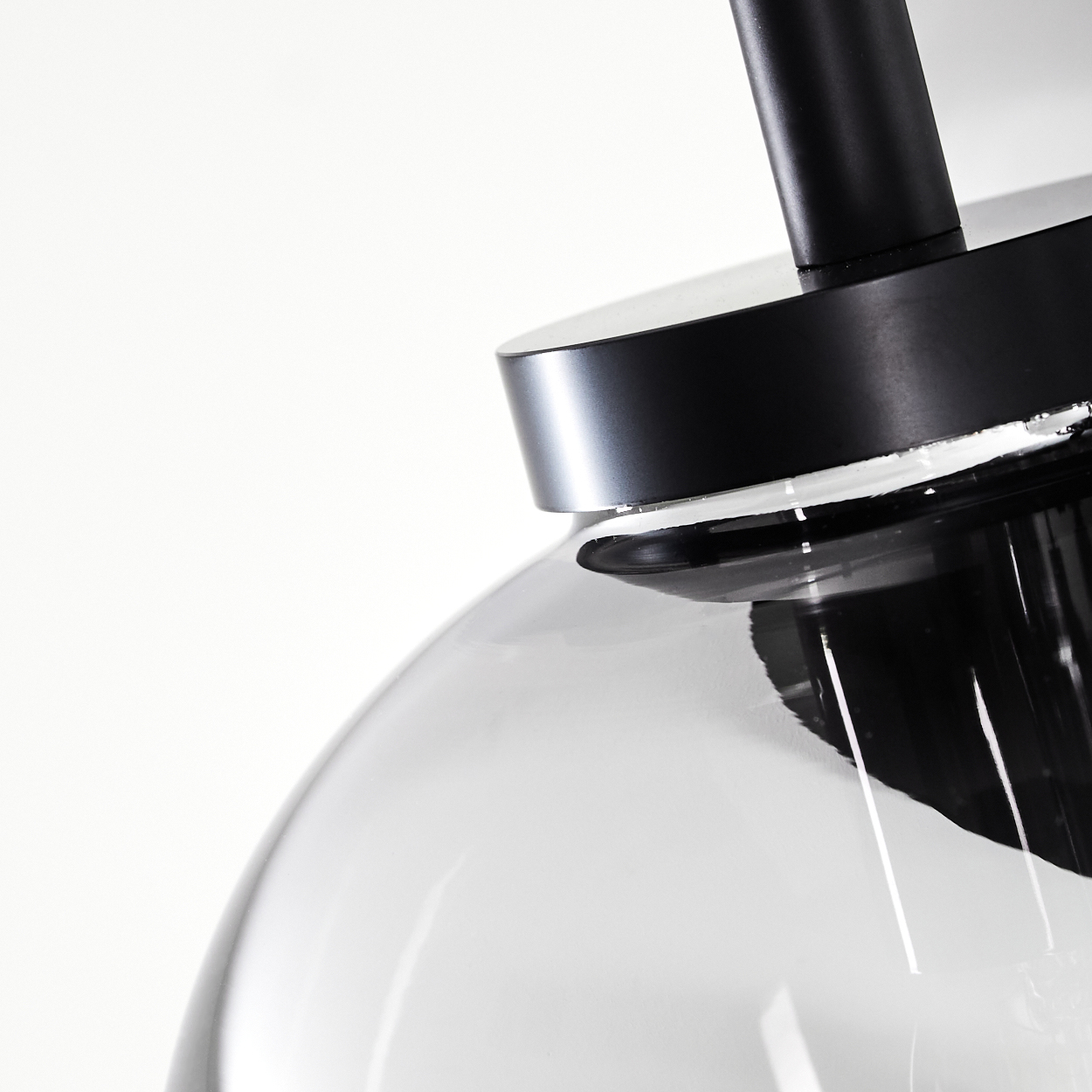 Nahaufnahme einer schwarzen und gläsernen Pendelleuchte. Das Glas ist klar und gebogen, mit schwarzem Metallsockel und Stiel auf weißem Hintergrund.