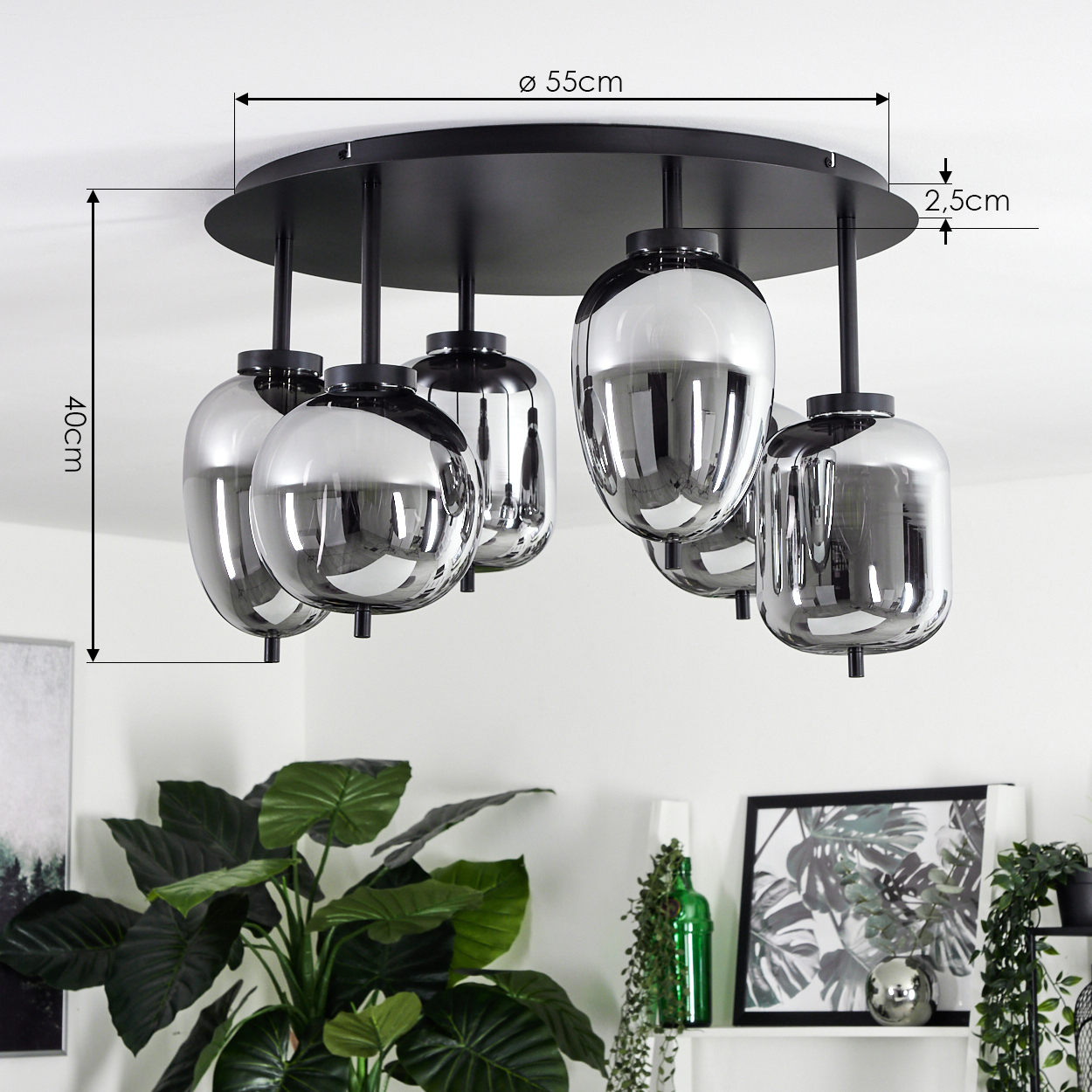 Eine moderne Deckenlampe mit fünf chromartigen Glasschirmen. Sie ist an einer schwarzen, kreisförmigen Basis befestigt. Grüne Pflanzen sind darunter zu sehen.