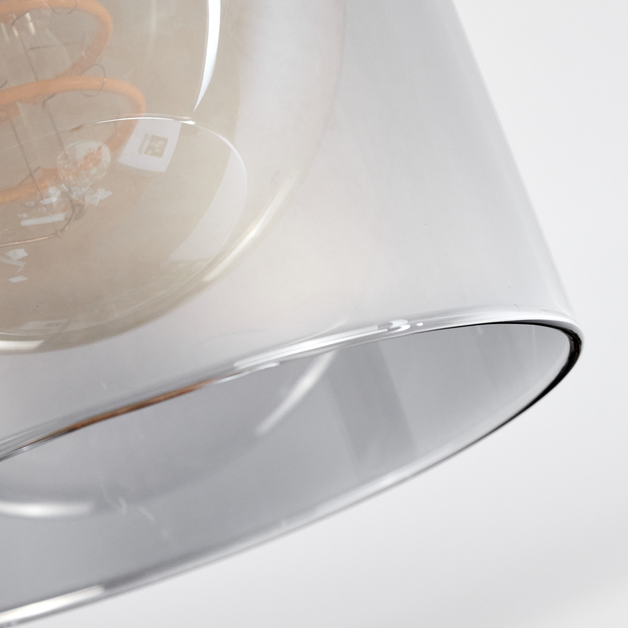 Nahaufnahme einer Lampe. Die Lampe hat einen durchsichtigen Glasschirm. Die Glühbirne ist sichtbar. Der Hintergrund ist weiß.
