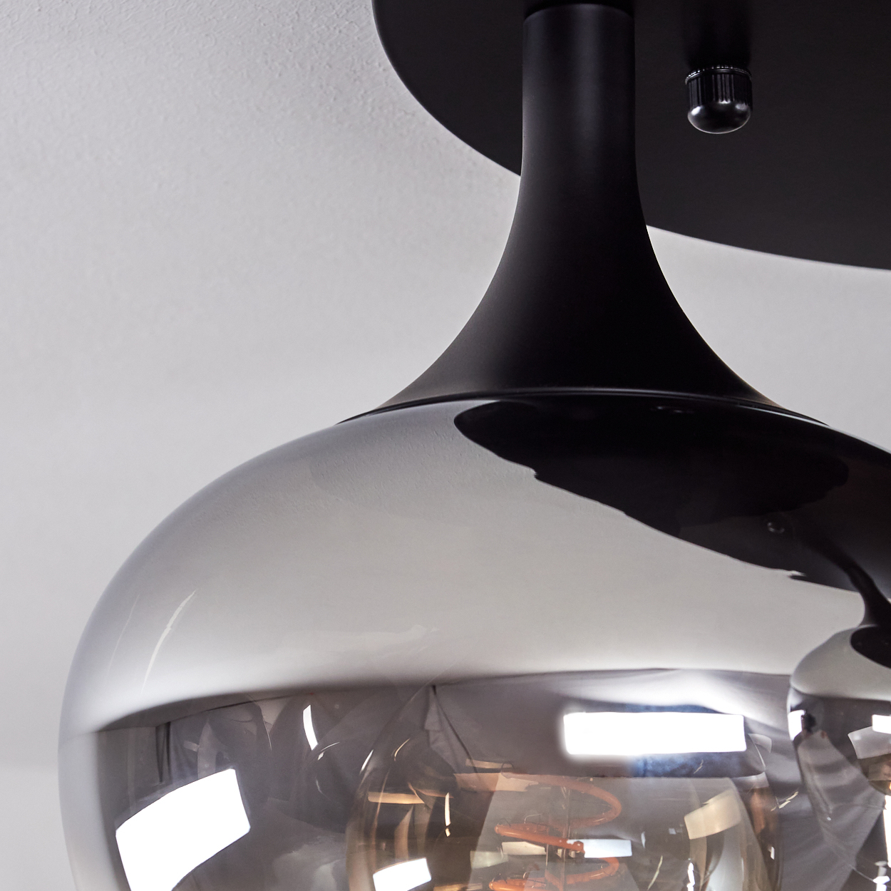 Nahaufnahme einer modernen schwarzen Deckenlampe mit rauchfarbenem Glasschirm. Die Lampe befindet sich vor einem weißen Deckenhintergrund.