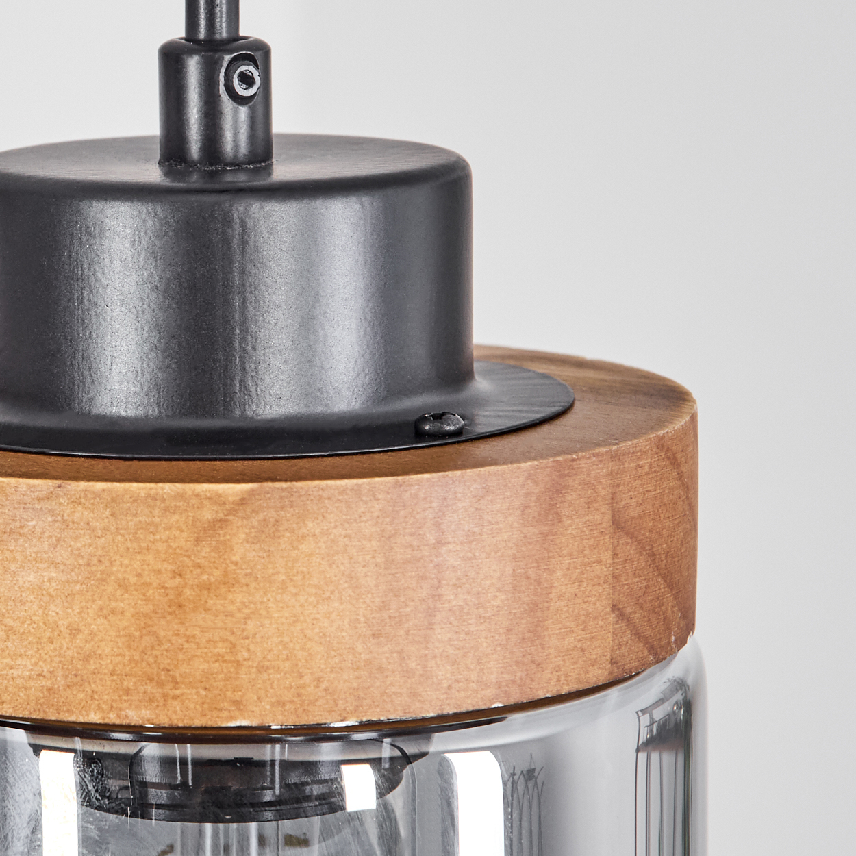 Nahaufnahme einer Lampe. Sie hat einen Holzsockel, einen schwarzen Metallaufsatz und einen Glasschirm, alles vor weißem Hintergrund.