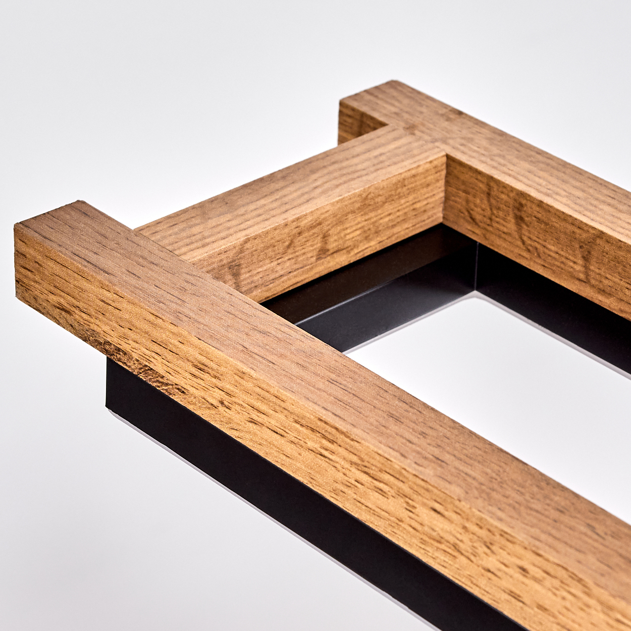 Nahaufnahme eines Holzrahmens mit einem schwarzen Metallinnenrahmen. Das Holz ist braun, der Hintergrund weiß.