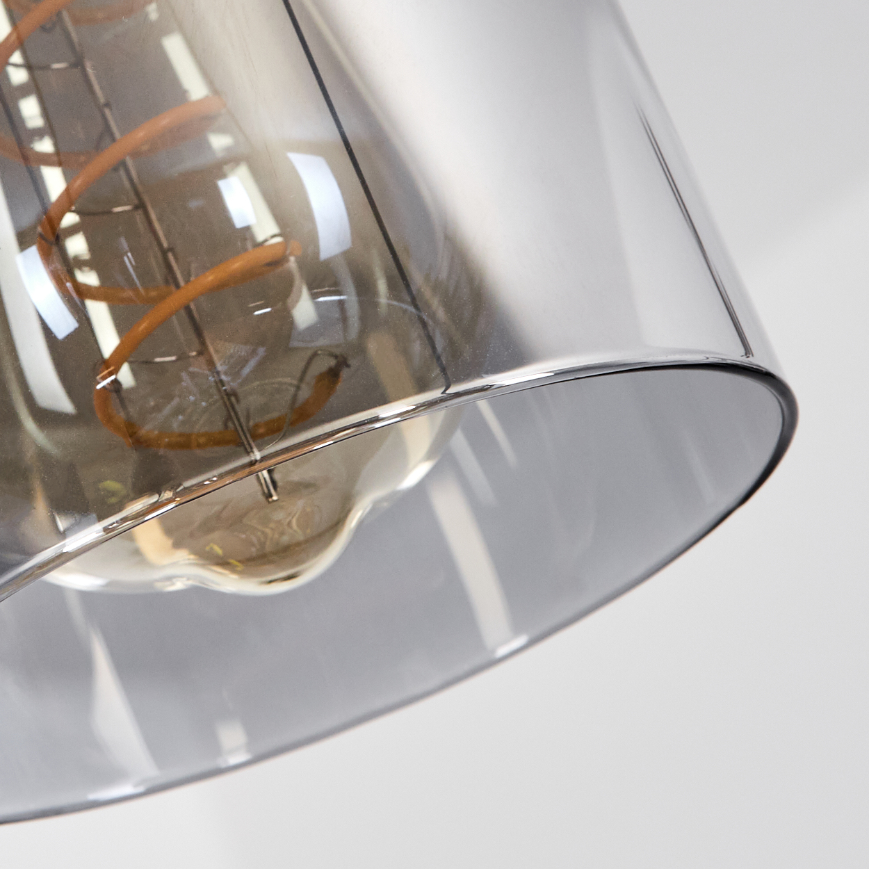 Nahaufnahme einer Glühbirne mit kupferfarbenem Glühfaden in einem transparenten, grau getönten Glasschirm vor weißem Hintergrund.