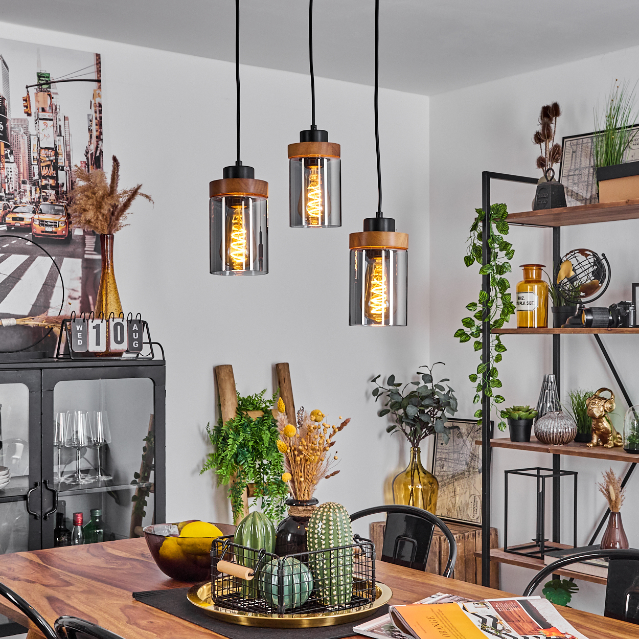 Esszimmer mit Holztisch, drei Hängelampen und dekorativen Gegenständen wie Vasen, Kakteen und einem Regal.