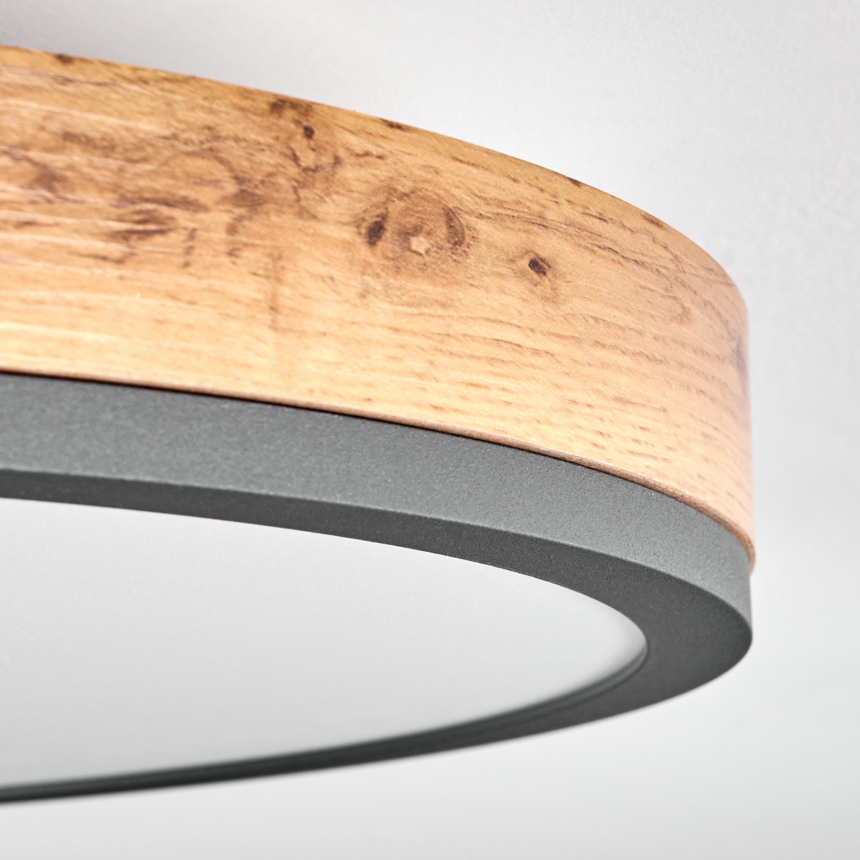 Nahaufnahme einer modernen Deckenlampe. Sie hat einen Holzring, ein dunkelgraues Metallband und eine weiße, kreisförmige Lichtquelle.