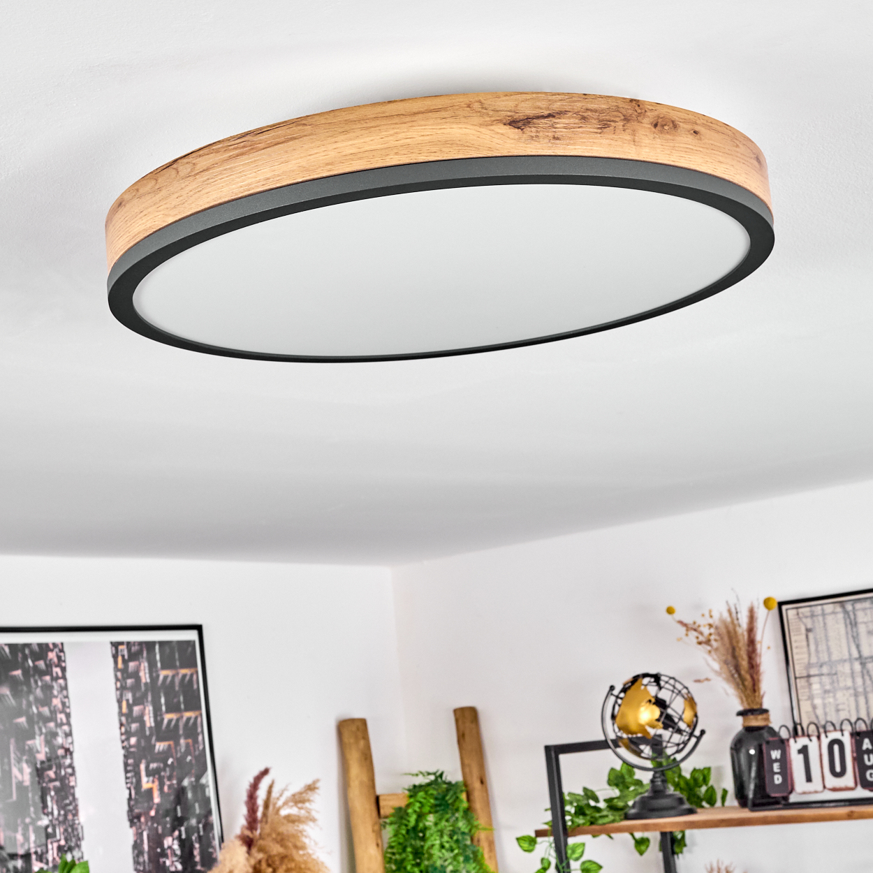 Eine Deckenleuchte mit Holzrahmen und schwarzem Rand. Das Licht ist oval. Im Hintergrund ein Raum mit Dekoration.