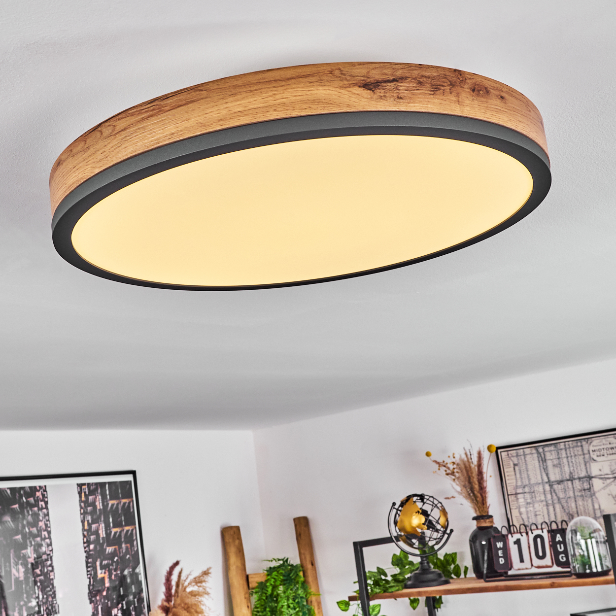 Eine ovale Deckenleuchte aus Holz mit schwarzem Rand. Die Lampe ist in einem Raum mit Dekoration eingeschaltet.