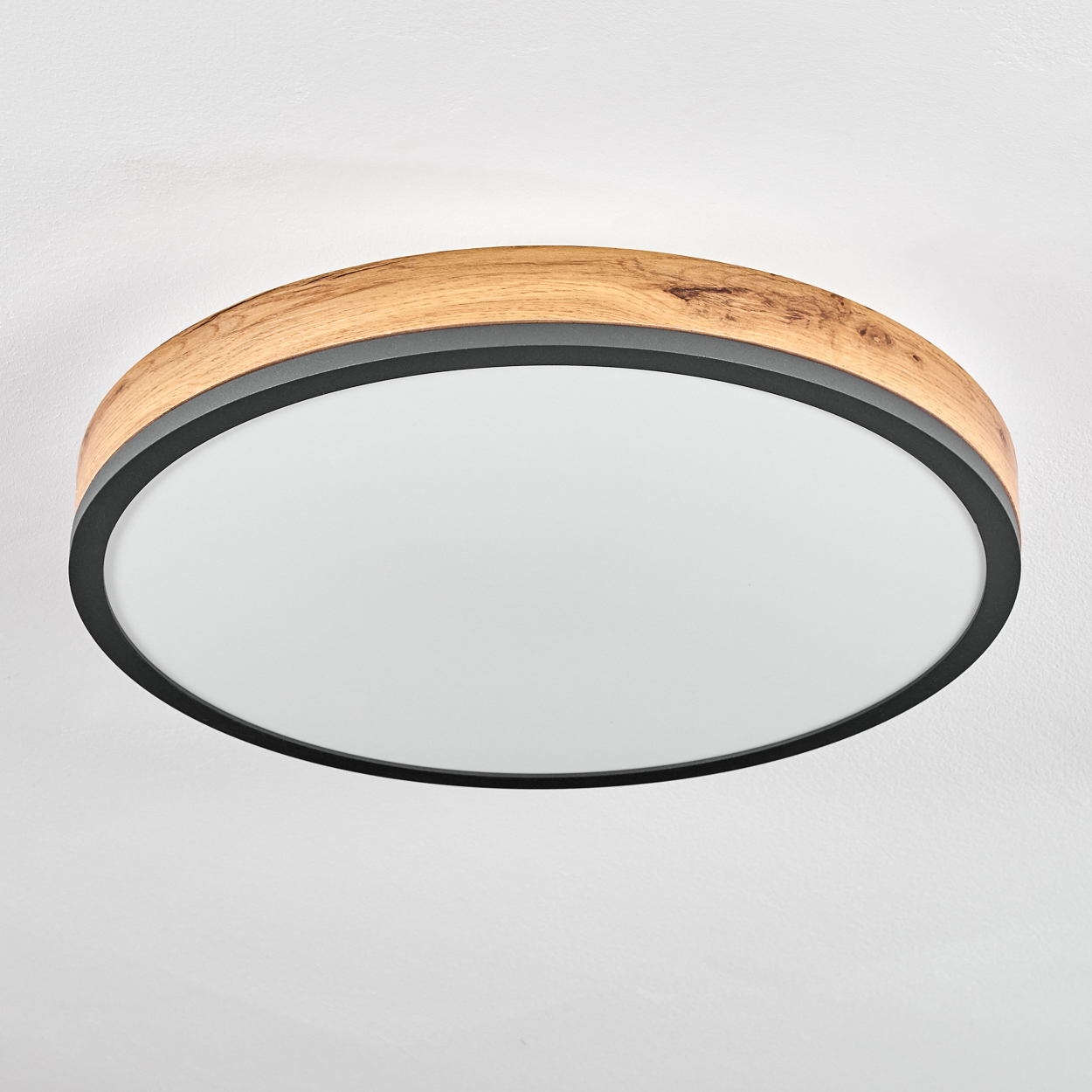 Eine runde Deckenleuchte. Sie hat einen äußeren Holzring, einen schwarzen Innenring und einen weißen Lichtdiffusor.