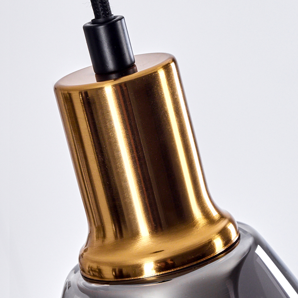 Nahaufnahme einer modernen Pendelleuchte. Sie hat einen goldenen Metallaufsatz, ein schwarzes Kabel und einen Glasschirm darunter.