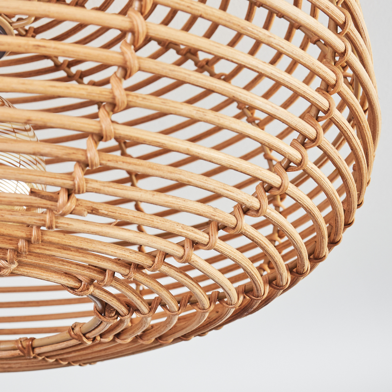 Nahaufnahme eines gewebten Lampenschirms aus Rattan. Das hellbraune Material bildet eine gekrümmte, offene Struktur mit einer sichtbaren Glühbirne.