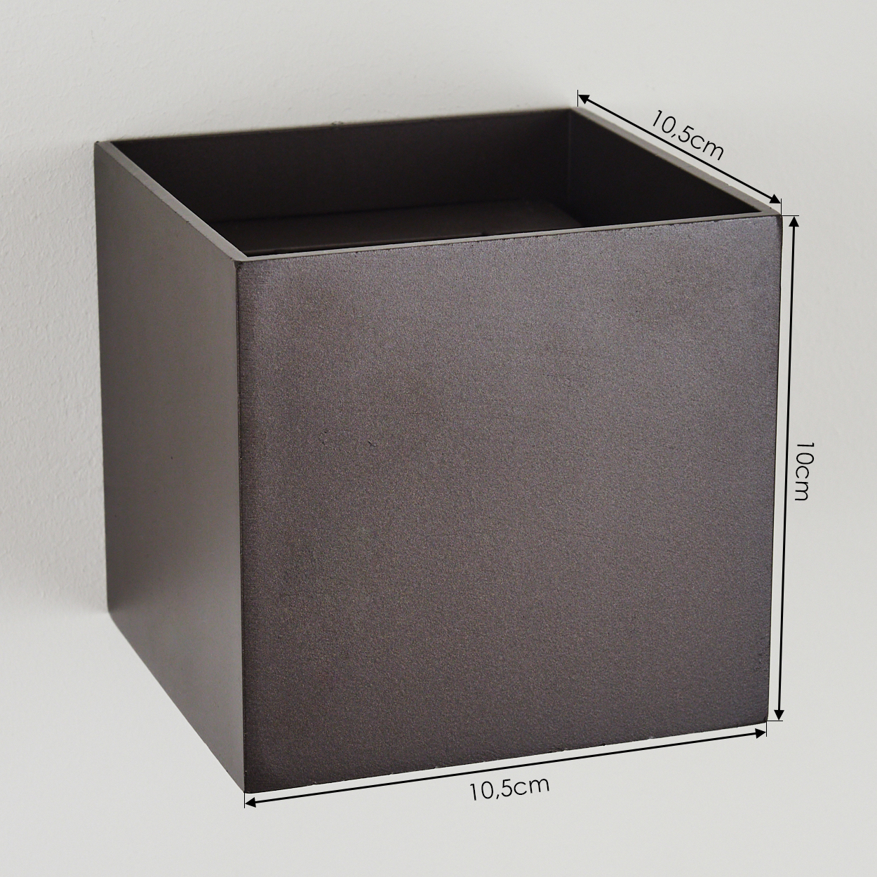 Ein dunkelbrauner, quadratischer Pflanzkasten ist an einer weißen Wand befestigt. Abmessungen sind beschriftet: 10,5 cm Seiten, 10 cm Höhe.
