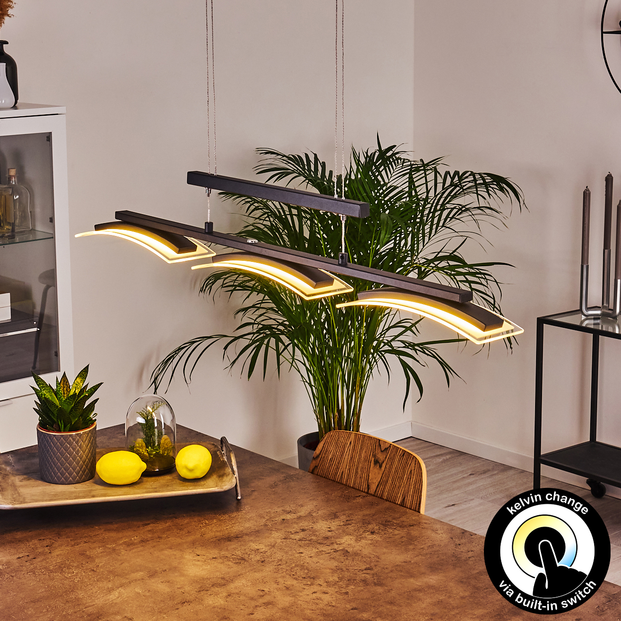 Moderne Hängelampe mit gebogenen Lichtern über einem Holztisch. Enthält Pflanzen, Zitronen und einen Kelvin-Wechselschalter.