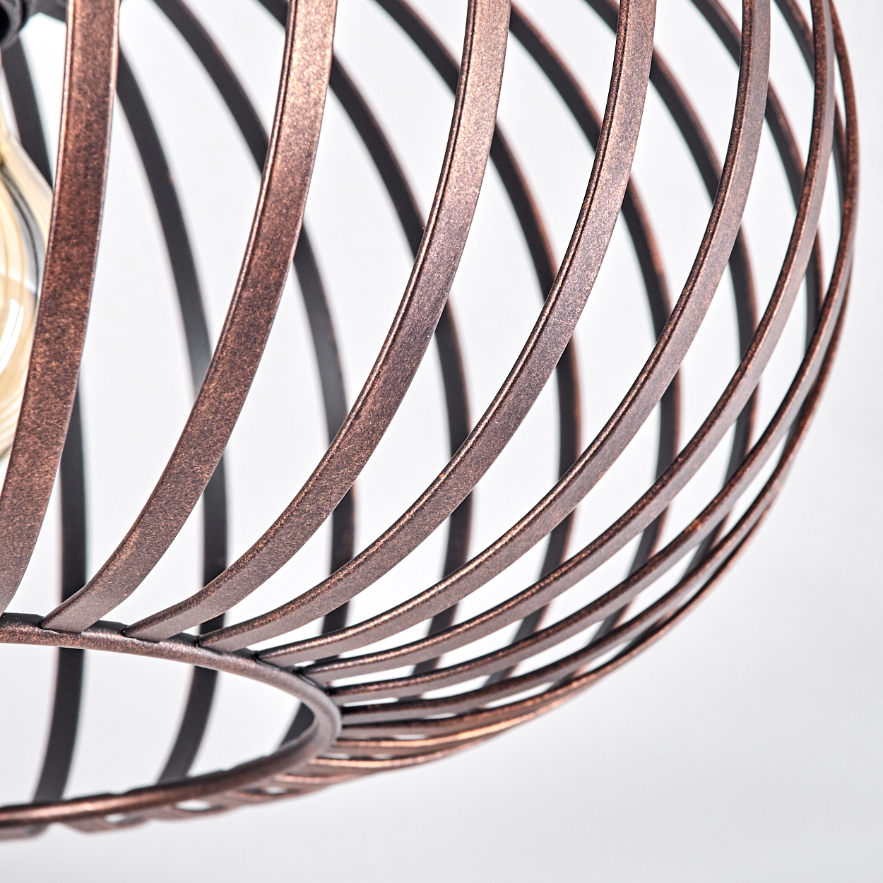 Nahaufnahme eines Lampenschirms aus Bronze. Die gebogenen Metallstäbe bilden eine Käfigform, im Inneren ist eine Glühbirne zu sehen.