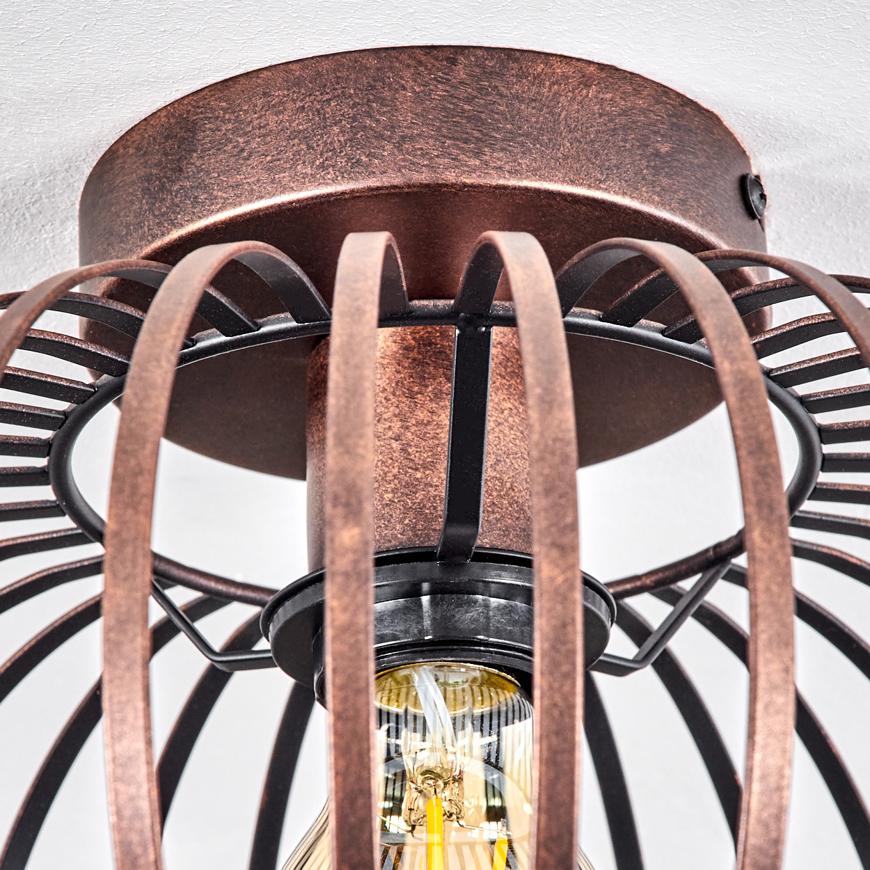 Nahaufnahme einer Deckenlampe im Vintage-Stil mit kupferfarbenem Käfigdesign. Eine Glühbirne ist sichtbar, die Decke ist weiß.