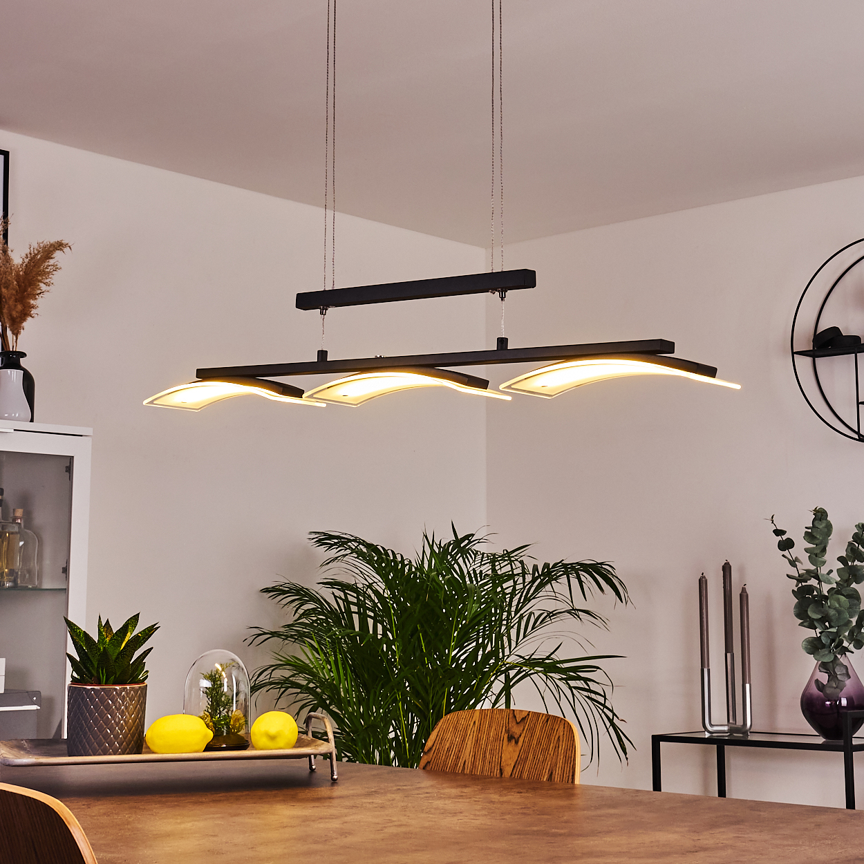 Ein modernes Esszimmer mit großem Holztisch, stilvollem Kronleuchter, Pflanzen und Dekoration. Der Raum hat eine warme, einladende Atmosphäre.