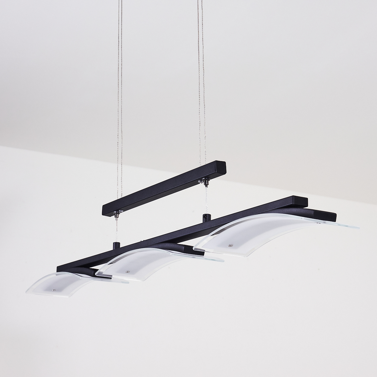 Eine moderne schwarze Leuchte mit drei gebogenen Glasschirmen hängt von der Decke. Der Hintergrund ist schlicht weiß.