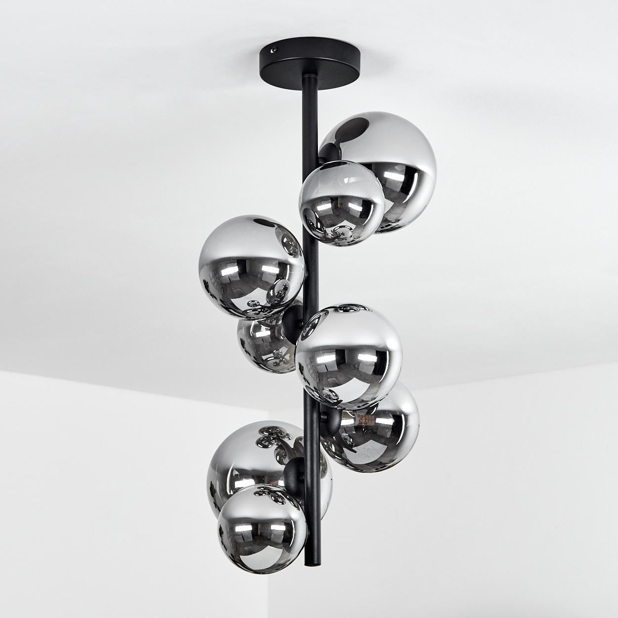 Eine moderne Hängelampe mit Chromkugeln hängt vor einer weißen Ecke. Die Kugeln reflektieren den Raum. Schwarze Stange und Deckenhalterung.