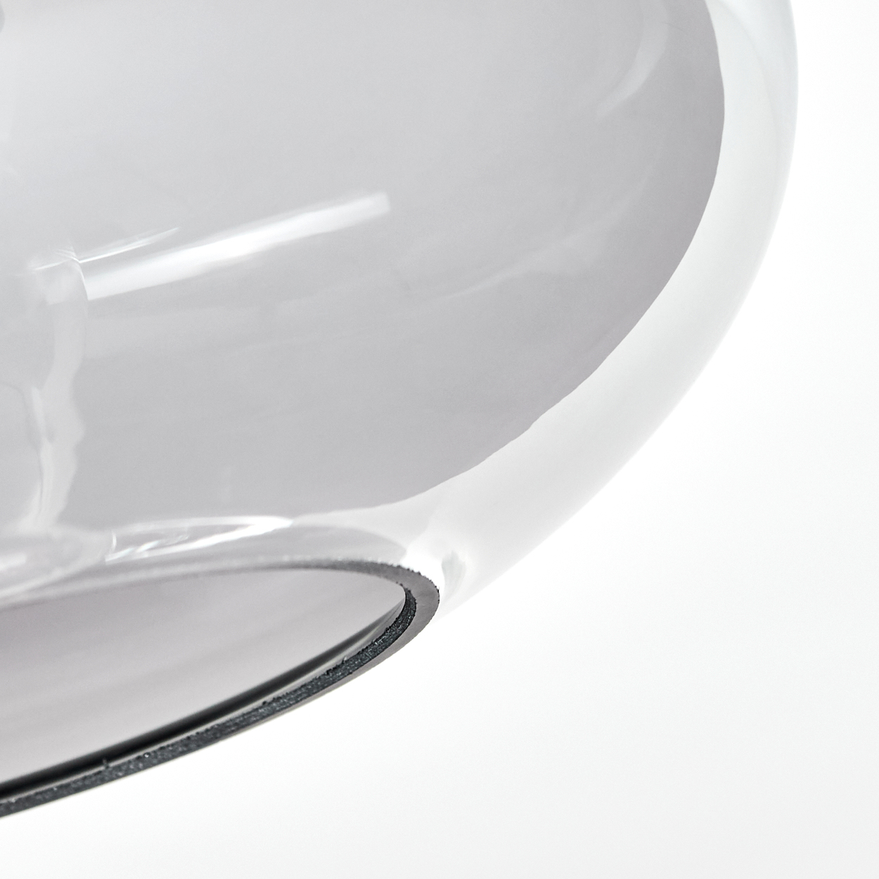 Nahaufnahme eines transparenten, grauen, gebogenen Glasobjekts vor weißem Hintergrund. Schwarze Kantendetails sichtbar.