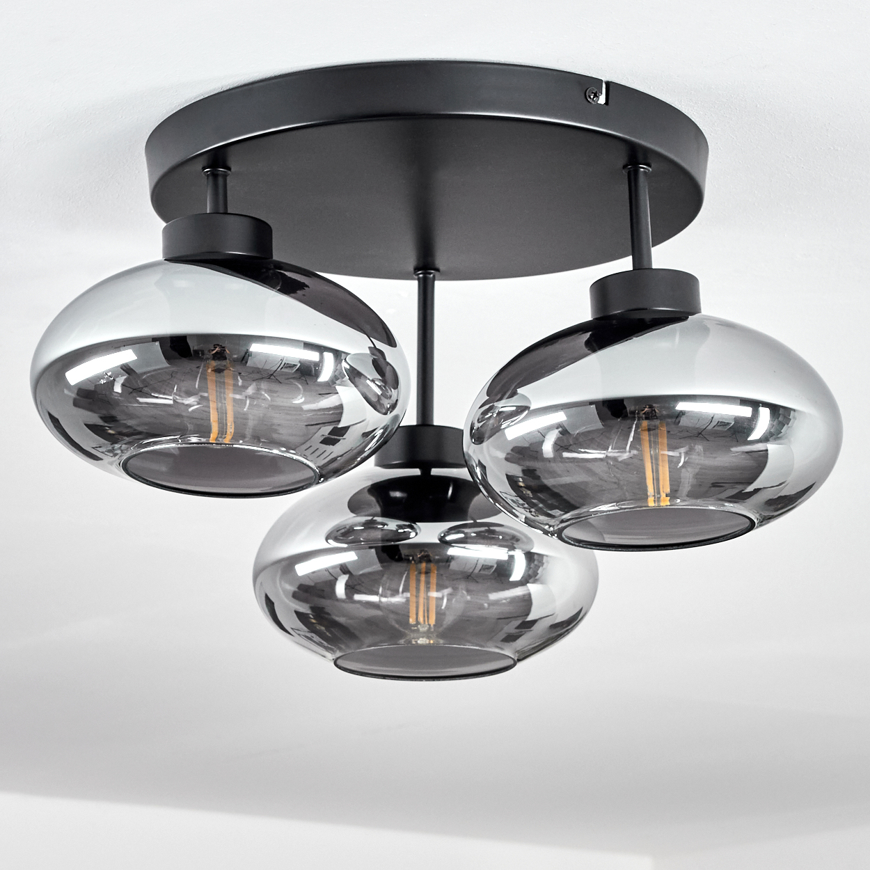 Eine moderne Deckenlampe mit drei rauchfarbenen Glasschirmen. Die Lampe hat einen schwarzen Sockel und Stiele und ist an einer weißen Decke angebracht.
