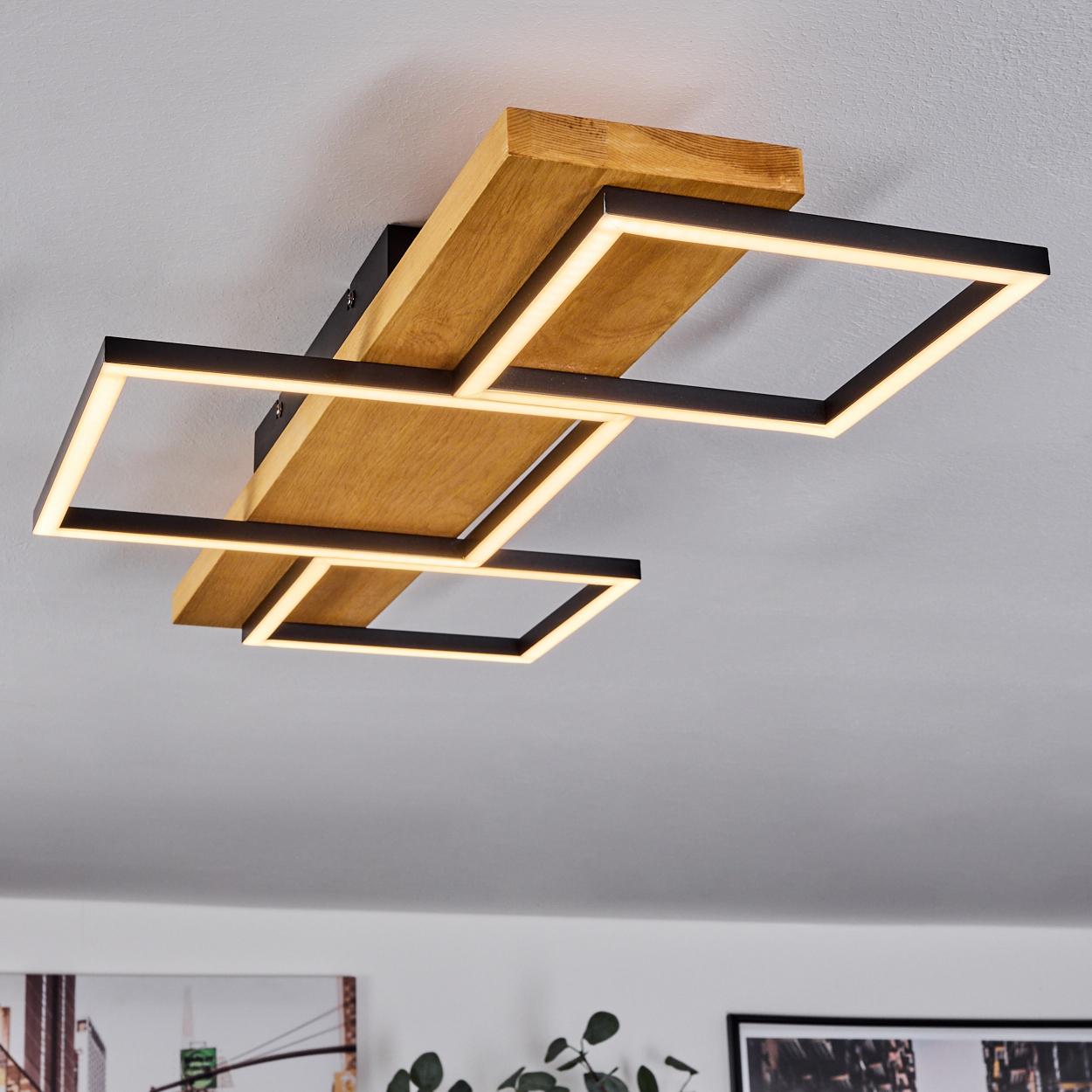 Eine moderne Deckenleuchte mit Holz- und schwarzen rechteckigen Rahmen, die warmes Licht aussendet. Die Decke ist weiß.