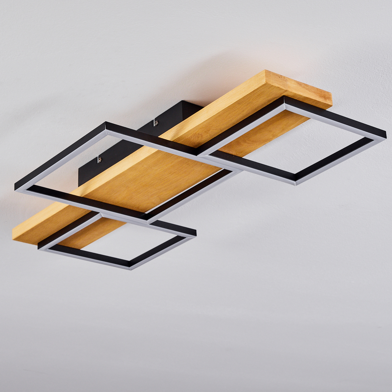 Moderne Deckenleuchte mit Holzsockel und schwarzen und silbernen Quadratrahmen vor einer weißen Decke.