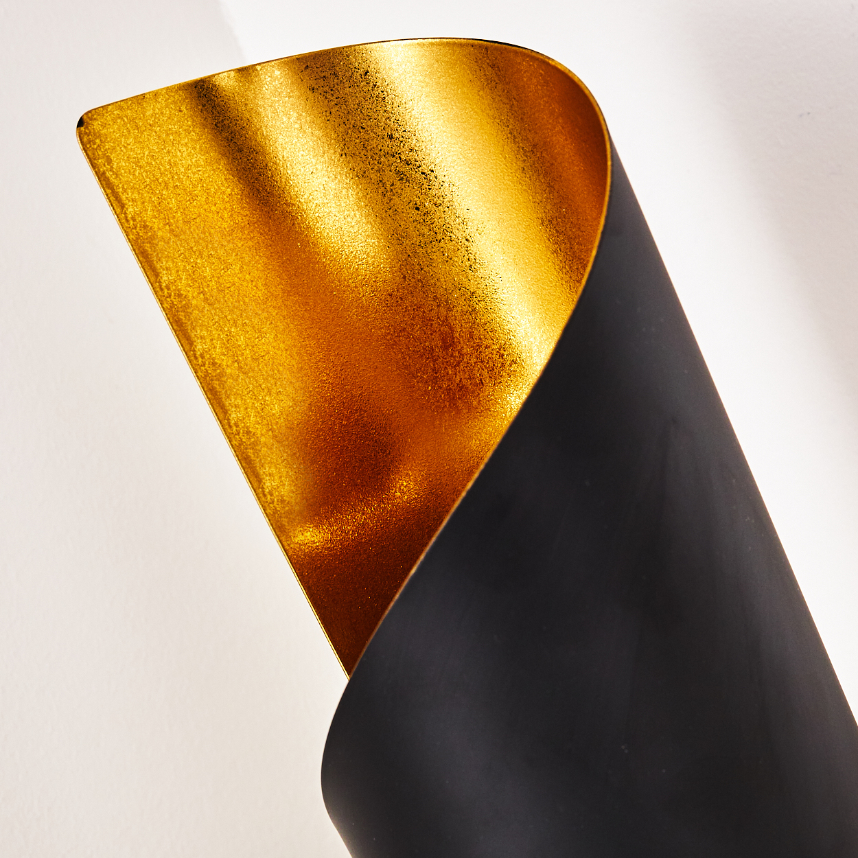 Ein goldfarbenes, gebogenes Objekt mit schwarzer Außenseite vor weißem Hintergrund. Die Goldoberfläche hat eine strukturierte Optik.