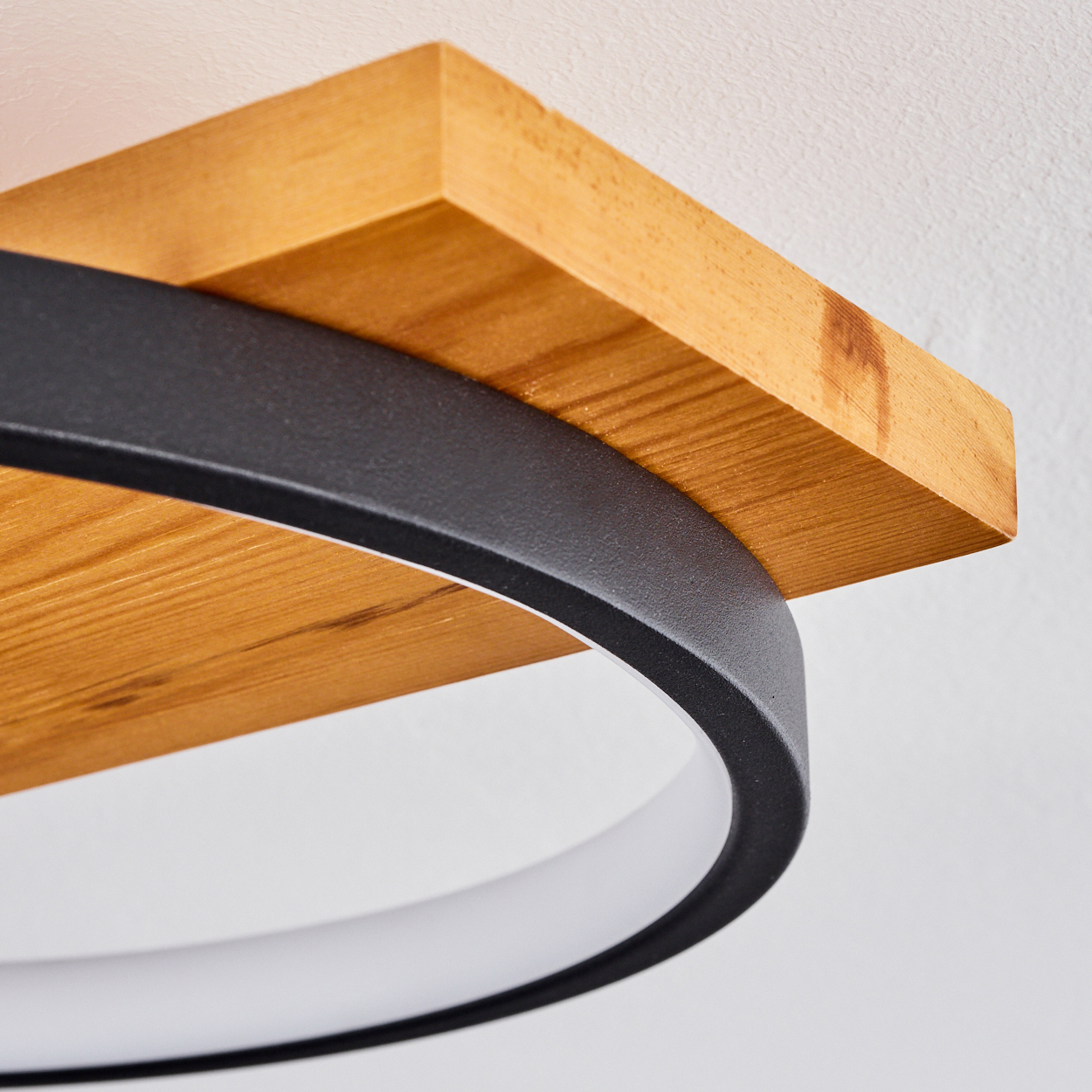 Nahaufnahme einer modernen Leuchte. Sie hat ein Holzregal, einen schwarzen Metallring und ein weißes Lichtelement vor weißem Hintergrund.