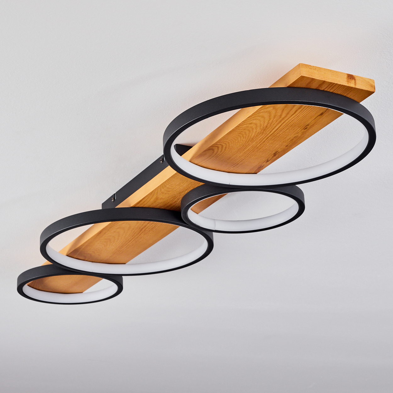 Eine Deckenleuchte. Sie hat drei schwarze kreisförmige Lichter mit weißen Innenringen, die auf einem Holzbalken montiert sind.