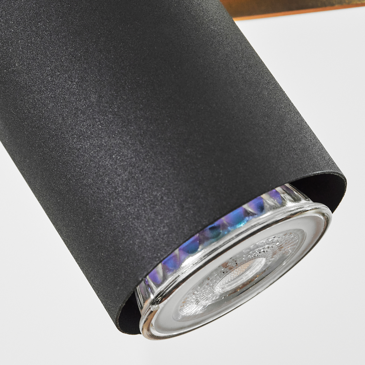Nahaufnahme einer schwarzen, zylindrischen Lampe. Die Lampe hat einen Metallsockel und eine klare Glühbirne, die verschiedene Farben reflektiert. Der Hintergrund ist weiß.