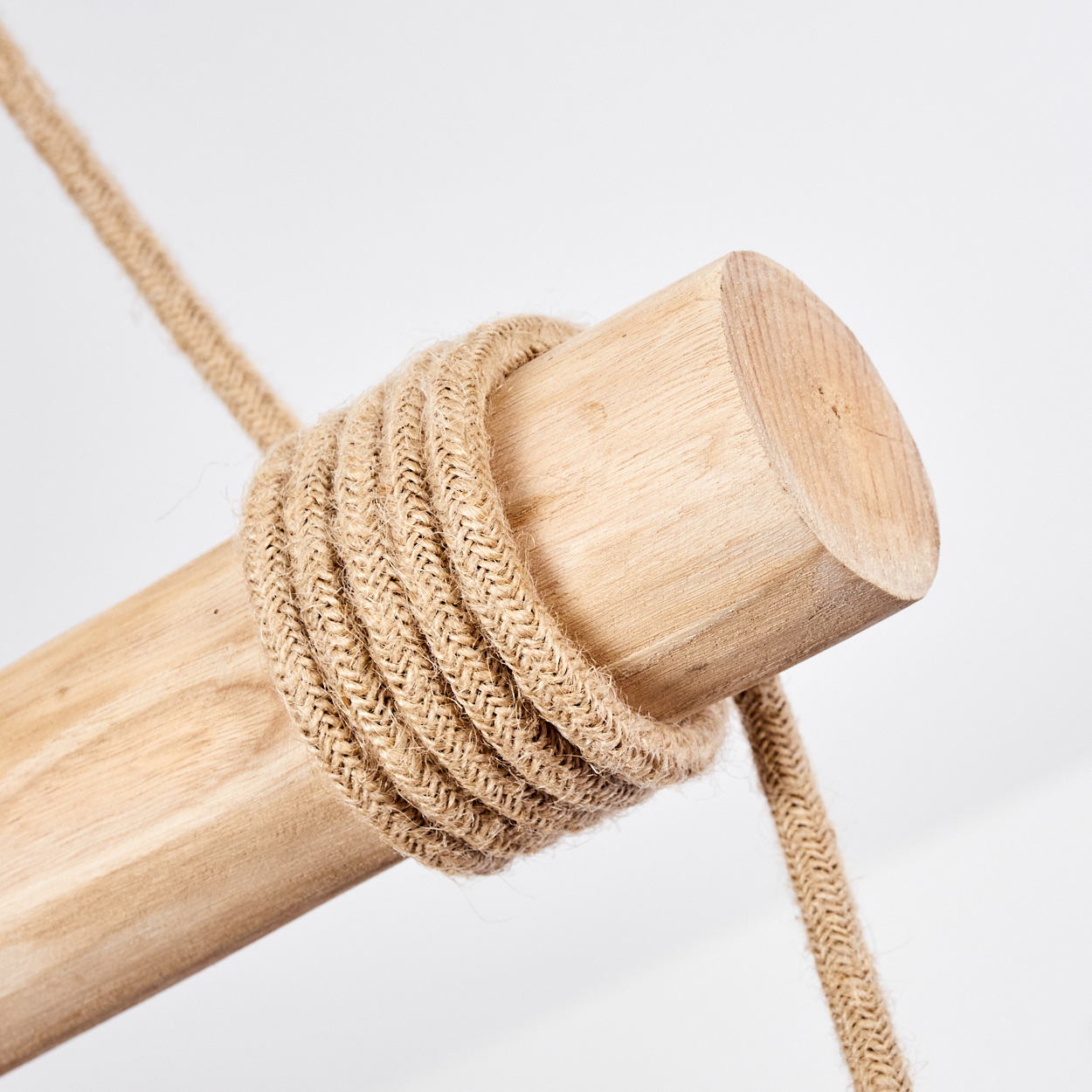 Holzzylinder mit Seil umwickelt. Helles Holz und Seil vor weißem Hintergrund. Das Seil ist eng um das Holz gewickelt.