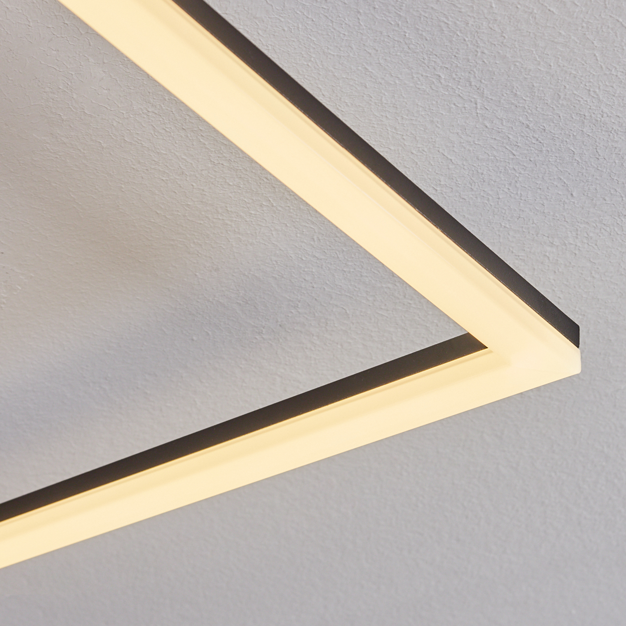 Eine rechteckige LED-Leuchte mit schwarzem Rahmen ist an einer strukturierten grauen Decke montiert. Das Licht ist an.