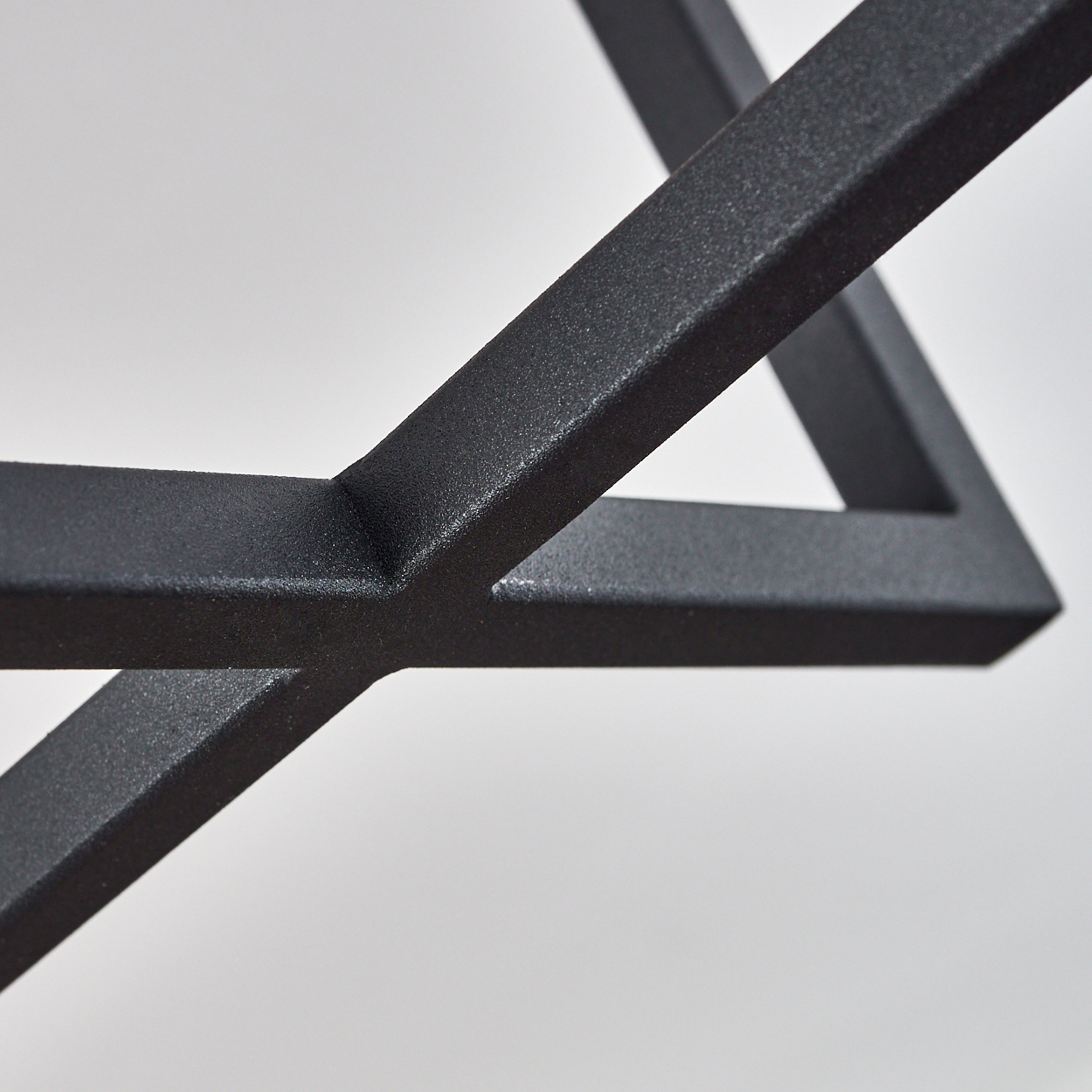 Nahaufnahme eines schwarzen Metallrahmens, der eine geometrische Form vor einem hellgrauen Hintergrund bildet. Der Rahmen hat eine strukturierte Oberfläche.